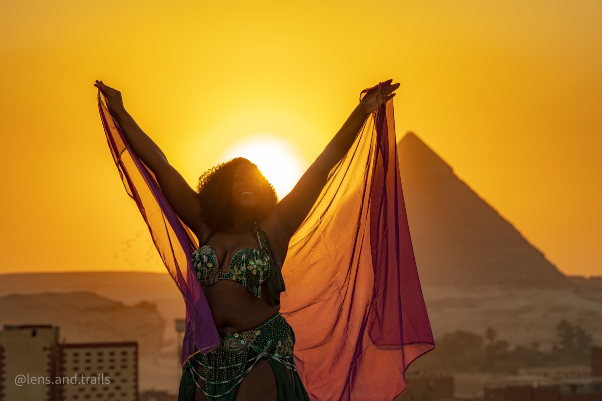 Dancer silhouetted against the Giza pyramid at sunset with a raised shawl