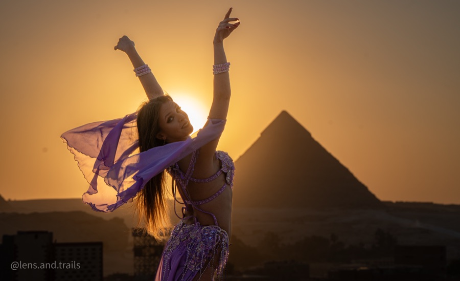 Dancer with arms raised in front of the pyramid at sunset