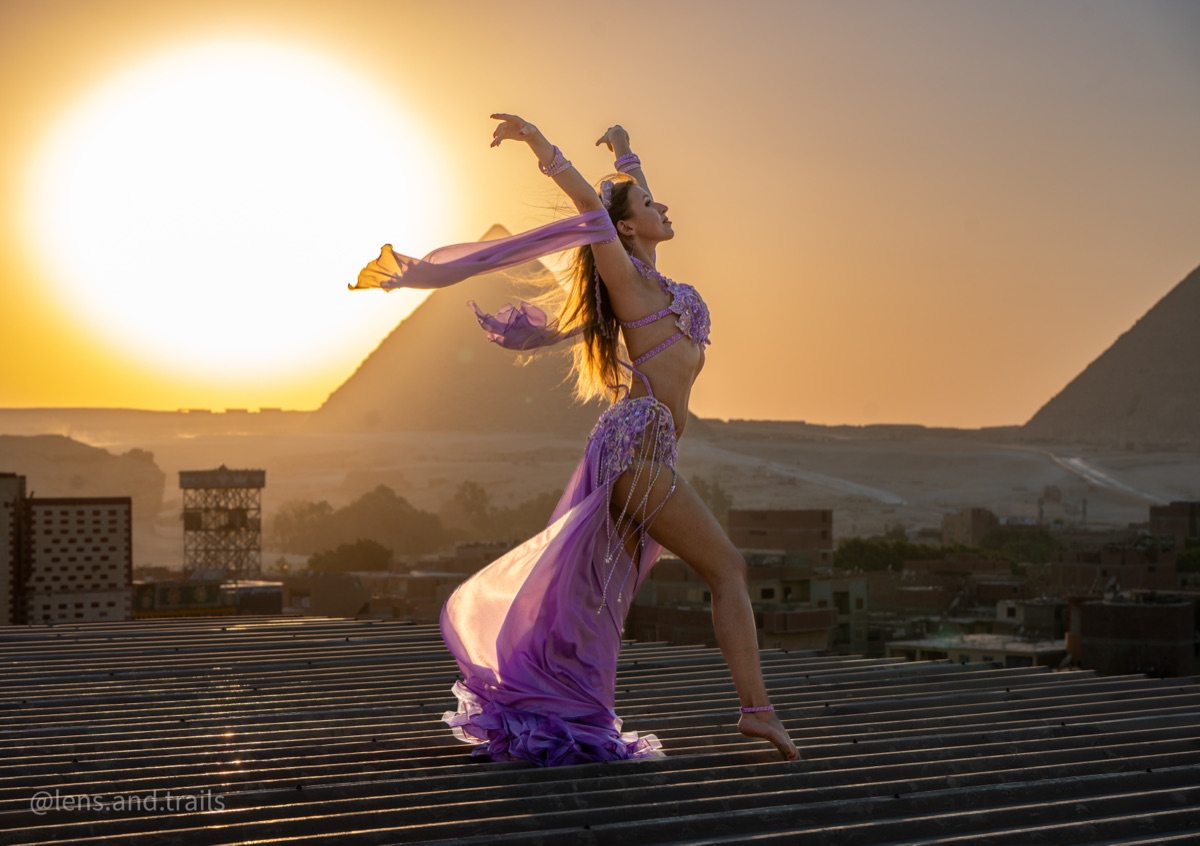 Dancer arched back on a rooftop with the pyramid and sunset behind