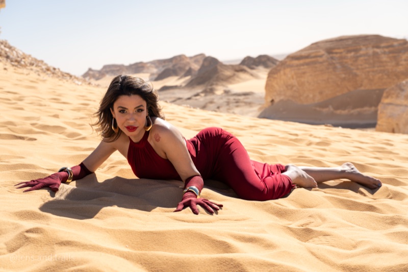 Dancer in a long red gown lying on golden desert sand in Egypt